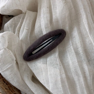 Detailed macro view of dark brown felt fabric oval BB hair clip on soft white textile background