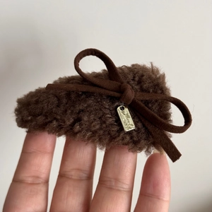 Detail of plush brown teddy bear hair clip with bow knot and metal tag held in hand