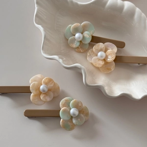 Detailed macro view of four floral acetate hair clips with pearls on a shell dish