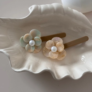 Elegant acetate flower hair clip with pearls and marble texture in a shell dish