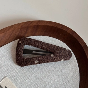 Detailed view of a brown polka dot woolen fabric triangle hair clip on a wood tray