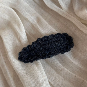 Close-up of a handmade wavy wool knit BB hair clip on a soft textured cotton fabric