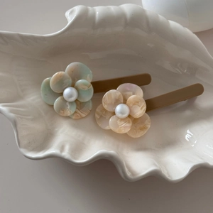Close-up of acetate floral hair clips with pearls on a decorative white shell tray