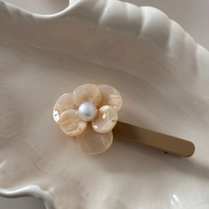 Close-up of floral acetate hair clip with pearl center on white shell ceramic tray