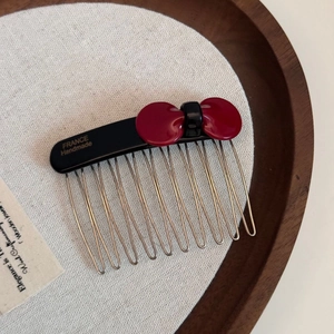 Detail of dark red acetate bow hair comb with silver metal teeth on a wooden tray