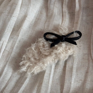 Detail of plush faux lambswool hair clip with a stylish black faux leather bow accent