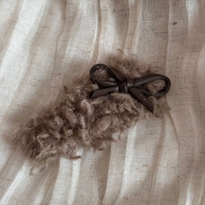 Detail of plush faux lamb wool hair clip with deep brown PU leather bow accessory