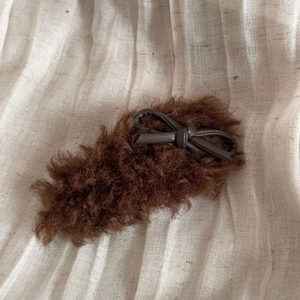 Detail showing faux shearling texture and dark brown PU leather bow on the plush hair clip