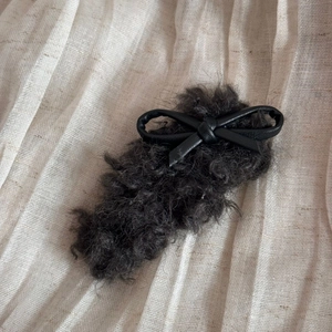 Detail of dark grey faux shearling hair clip with a black PU leather bow decoration