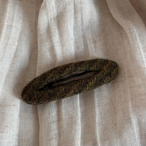 Close-up of vintage moss green tweed fabric wrapped hair clip with textured wool finish