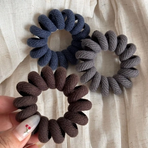 Close-up of ribbed fabric spiral hair ties in navy, dark grey and brown tones