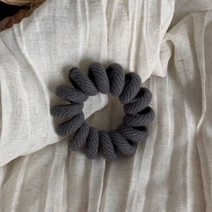 Close-up of dark grey spiral hair tie with twill fabric texture on linen surface