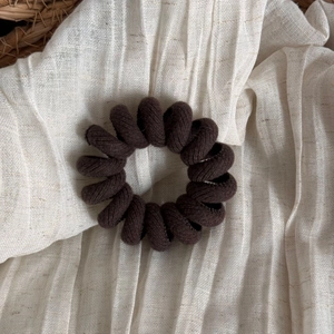Detail of dark brown fabric spiral hair tie on a soft textured cream cloth background