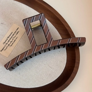 Detail of large brown resin hair claw clip with blue and white stripes on wood tray