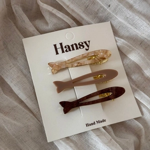 Three acetate fish-shaped hair clips in marble and pink tones on a display card