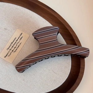 Detail of coffee brown shark hair clip with silver horizontal stripes on wooden tray