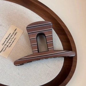 Detailed view of large brown striped hair claw clip with walnut wood texture on a tray