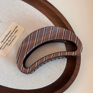 Detailed close-up of a brown striped resin hair claw clip on a rustic linen tray