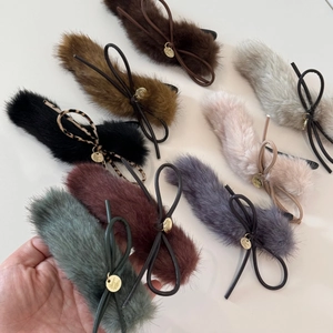 Detail of plush faux fur hair clip featuring leather bow and round gold charm