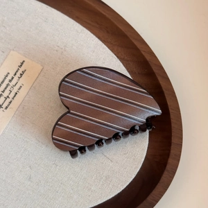 Detailed view of heart-shaped hair claw with blue stripes on a warm beige fabric