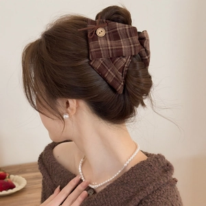 Detailed view of a brown plaid bow hair claw clip with a wooden button on a model