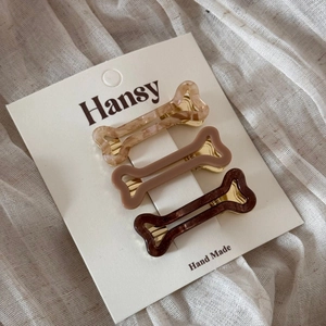 Three bone-shaped acetate hair clips in brown tones on a white display card detail