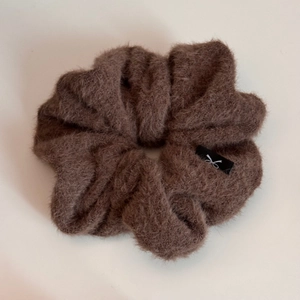 Détail d'un chouchou en peluche marron foncé avec texture en fausse fourrure et étiquette