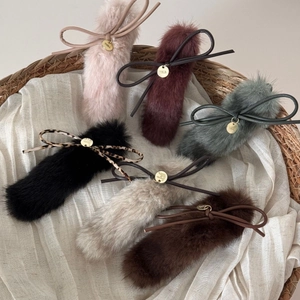 Plush bow hair clips in multiple colors with gold label charms on a white fabric background