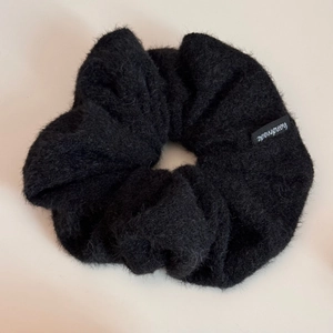 Détail d'un chouchou noir en peluche avec étiquette et texture douce en simili mohair