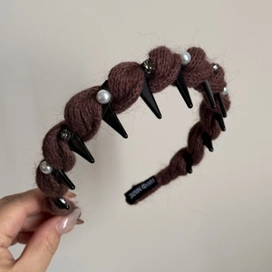 Detail einer braunen Strick-Haarklammer mit Perlen, Nieten und Handgefertigt-Etikett