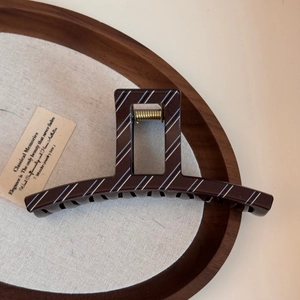 Close-up of a large brown hair claw clip with blue stripes on a wooden tray