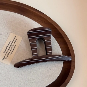 Close-up of deep brown resin hair claw with white stripes in a wooden tray