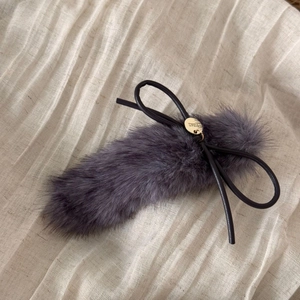 Close-up of grey plush hair clip with a black leather bow and gold metal logo tag