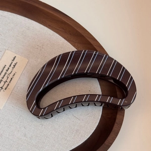 Close-up of brown striped large hair claw clip on a minimalist wooden tray display
