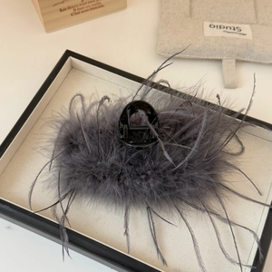 Dettaglio dell'elegante molletta per capelli con piume grigie su vassoio beige con luce soffusa