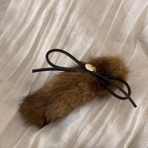 Close-up of soft brown plush hair clip featuring a black bow and gold brand plaque