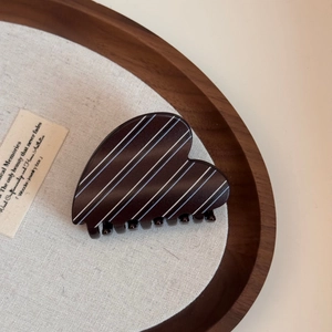 Macro detail of a heart-shaped dark brown hair claw clip with elegant white stripe pattern