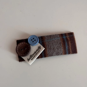 Detail of a brown herringbone fabric hair clip with decorative buttons and woven label tag
