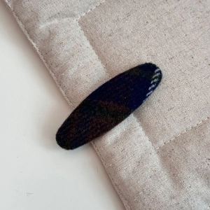 Vue détaillée d'une pince à cheveux en laine à carreaux foncés sur un tissu beige texturé