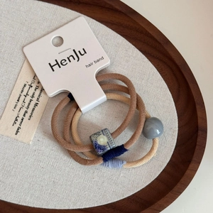 Dettaglio di tre elastici per capelli con perle di ceramica blu su vassoio di legno