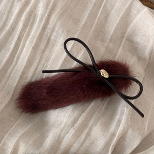 Close-up of wine red plush hair clip featuring a black bow and gold metallic pendant detail