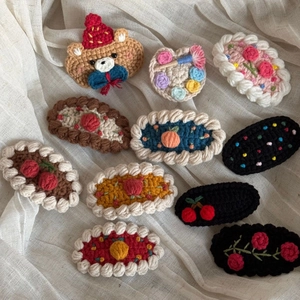 Detailed close-up of ten handmade crochet hair clips featuring cute cartoon animal and fruit motifs