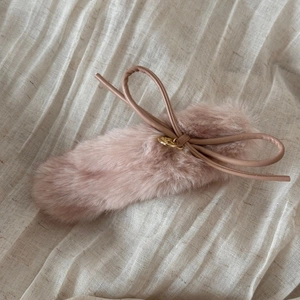 Close-up of pink faux fur hair clip featuring a leather bow and golden metal charm