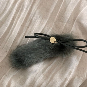 Detail of plush dark blue hair clip with black bow and gold logo tag on beige fabric