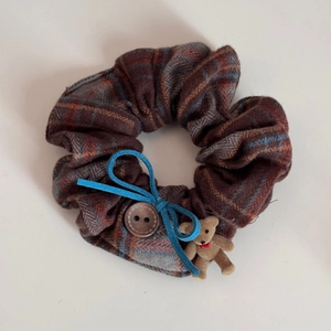 Detail of checkered fabric scrunchie with a blue bow, wooden button and small bear charm