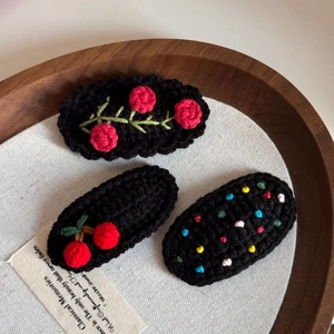 Detail of three handmade crochet hair clips featuring red roses and cherries in a wooden tray