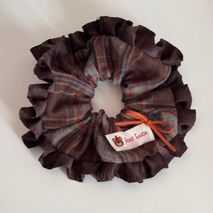 Macro detail of a large brown satin scrunchie with orange bow and Good Luck label