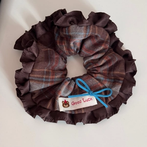 Detail of checkered fabric scrunchie with brown ruffled edges and a blue suede bow