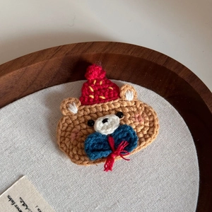 Close-up of handmade crochet bear hair clip with a red wool hat and blue bow detail