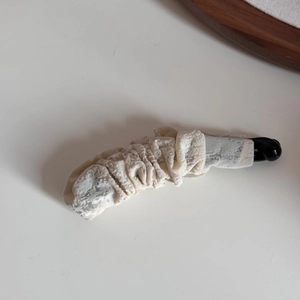 Détail de la texture en tissu plissé blanc crème sur une pince à cheveux banane rétro